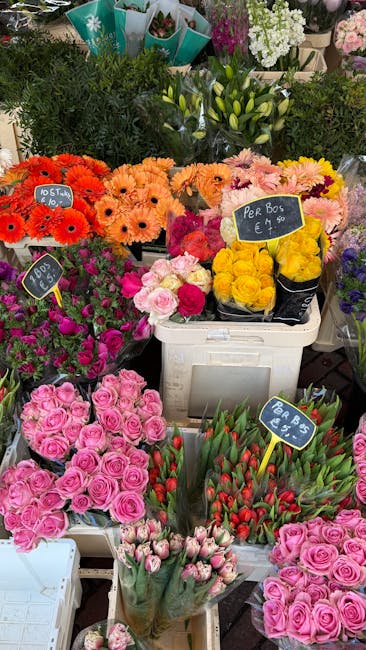 A vibrant display of fresh flowers at a floral market, featuring various bouquet arrangements and individual blooms. In the foreground, there are multiple pink roses with tightly packed petals, some w