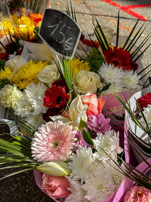 A vibrant floral arrangement featuring a mix of fresh flowers including pink gerbera daisies, white roses, red gerbera daisies, and white chrysanthemums, all arranged with green foliage and blades of