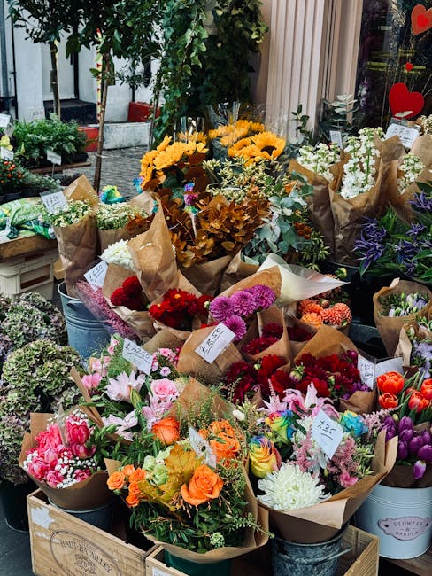A vibrant display of fresh floral bouquets arranged outdoors on a flower stall, featuring a variety of colorful flowers including yellow sunflowers, pink and orange roses, purple irises, white lilies,